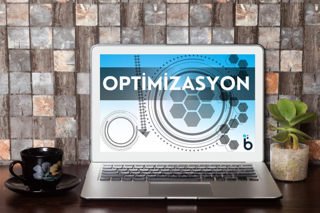 Ahşap bir masanın üzerinde "Optimizasyon" kelimesinin yazdığı bir dizüstü bilgisayar.