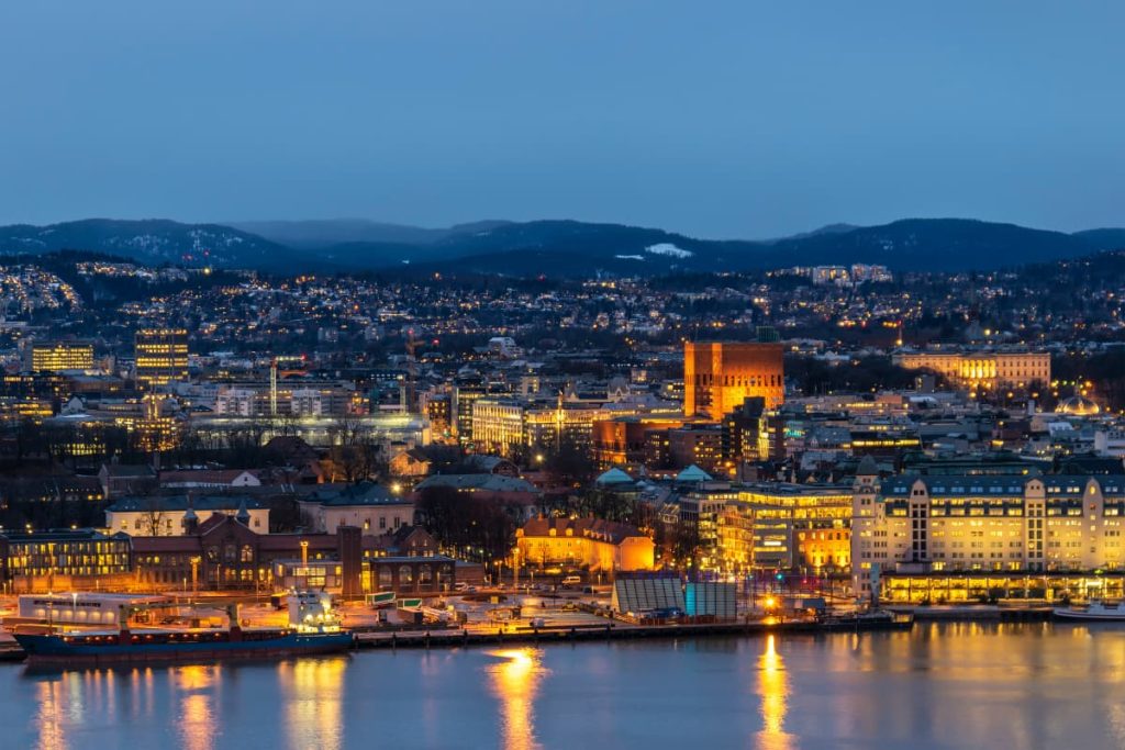 An aerial view of Oslo, Norway, at night, showcasing the city's waterfront and the Oslo City Hall.